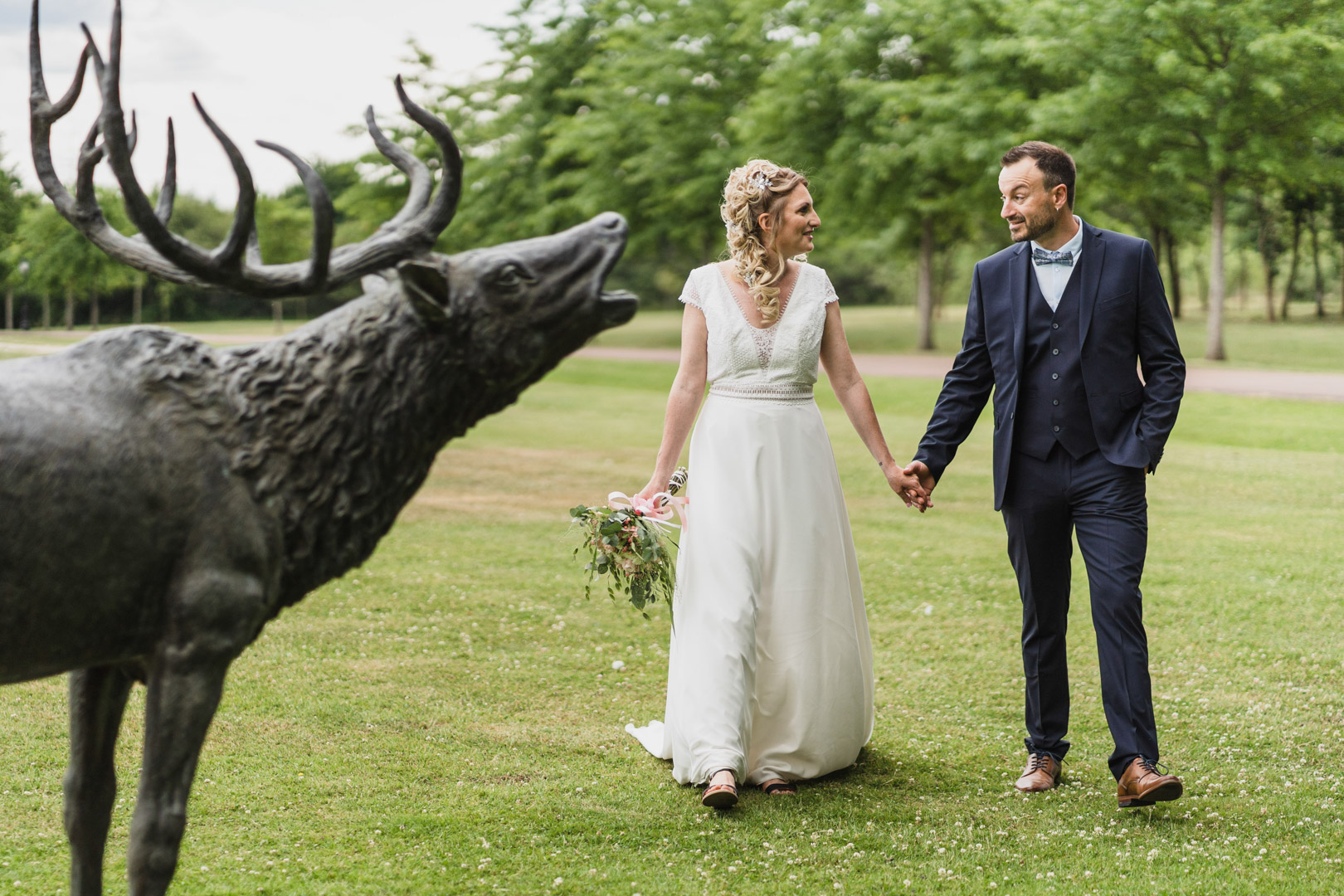 couple de mariés qui se promene main dans la main à coté de la statue d'un cerf qui brame